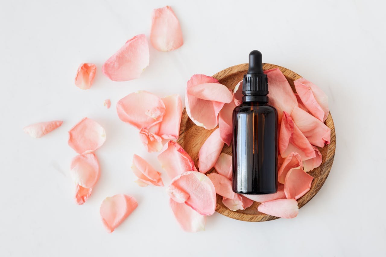 about-01 Top view of empty brown bottle for skin care product placed on wooden plate with fresh pink rose petals on white background isolated